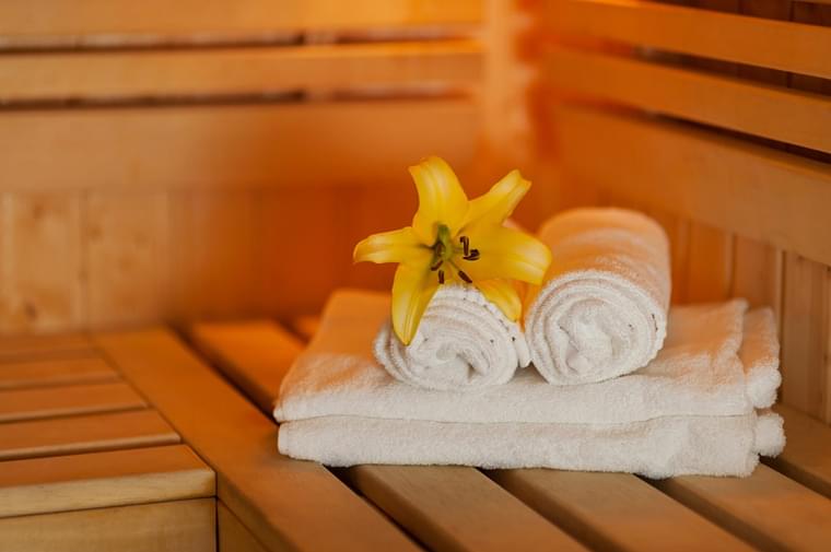 A cozy sauna room with fluffy towels and a cheerful yellow flower.